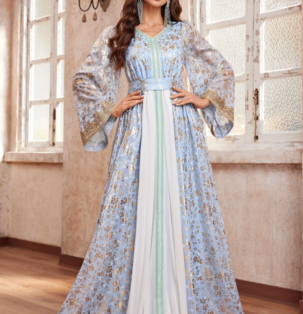 A woman models a traditional long dress with wide bell sleeves, featuring a light blue and gold floral pattern, a white center panel, and a mint green patterned vertical stripe down the front.